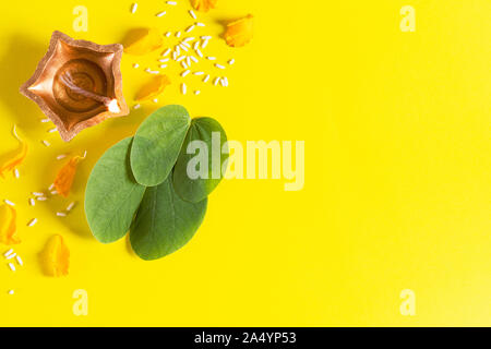 Happy Dussehra. Les lampes d'argile Diya Dussehra allumé pendant avec des fleurs jaunes, vert feuille et du riz sur fond jaune. Festival indien de Dussehra concept. Banque D'Images