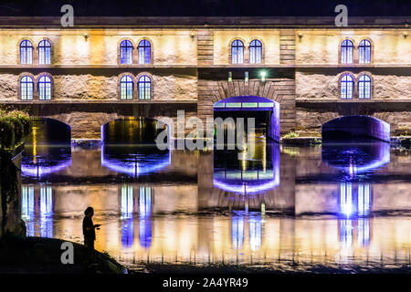 Silhouette d'un homme à la pêche à la nuit en face de l'allumé Barrage Vauban, un travail défensif sur l'Ill dans le quartier historique de la Petite France. Banque D'Images