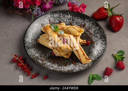 Rouleaux de crêpes à la banane-chocolat dragées dans une assiette sur un fond gris Banque D'Images