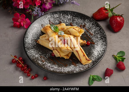 Rouleaux de crêpes à la banane-chocolat dragées dans une assiette sur un fond gris Banque D'Images