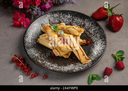 Rouleaux de crêpes à la banane-chocolat dragées dans une assiette sur un fond gris Banque D'Images