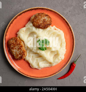 Purée de pommes de terre et côtelettes de viande dans une plaque orange sur fond gris Banque D'Images