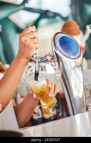 Nous rencontrez l'Oktoberfest. Main de bartender pouring une grande bière blonde au robinet. Servir la bière pour client. Vue latérale du jeune bartender pouring beer bien que sta Banque D'Images