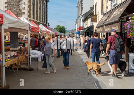 Les touristes les visiteurs marchant le long des stands extérieurs du marché du jeudi à l'été Market Square Keswick Cumbria Angleterre Royaume-Uni Grande-Bretagne Banque D'Images