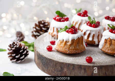 Noël petits gâteaux avec du sucre glace bundt et de groseilles sur une tranche de bois rustique avec des lumières de Noël sur l'arrière-plan Banque D'Images