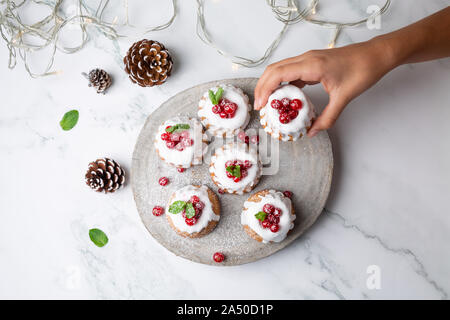 Femme cueillette à la main de petits gâteaux de Noël avec glaçage sucre bundt et de groseilles sur une tranche de bois rustique. Vue d'en haut Banque D'Images