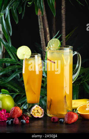 Cocktail mangue ananas dans une cruche en verre et sur un fond sombre avec des fruits : ananas, mangue, fraise, de la purée de mangue, ananas, pêche, pomme Banque D'Images