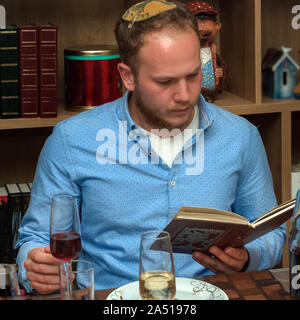 La célébration de la famille juive Pâque.homme juif se lit de la Haggadah alors qu'ils célèbrent le Seder. La fête est célébrée le premier soir de la Pâque, maison de vacances commémorant l'exode des Juifs d'Egypte. Banque D'Images