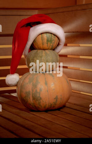 Une pyramide de trois citrouilles sur une surface en bois est orné d'un chapeau de Père Noël. À travers les murs en lattes de bois lumière transperce avec beaut Banque D'Images