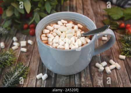 Mug gris avec boisson chocolat garnies de petits blancs les guimauves et le chocolat et la cannelle en poudre sur le bureau en bois avec décor d'hiver arrangement Banque D'Images