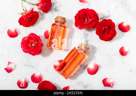 L'eau de rose parfumée dans le flacon en verre et de petites roses rouges de pétales . Massage, aromathérapie et cosmétiques bio concept Banque D'Images