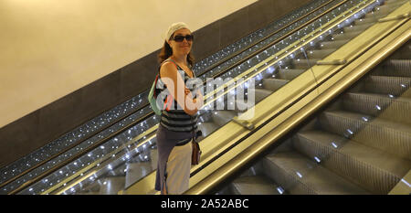 Jeune femme avec des lunettes de soleil sur échelle mobile dans le centre commercial moderne Banque D'Images