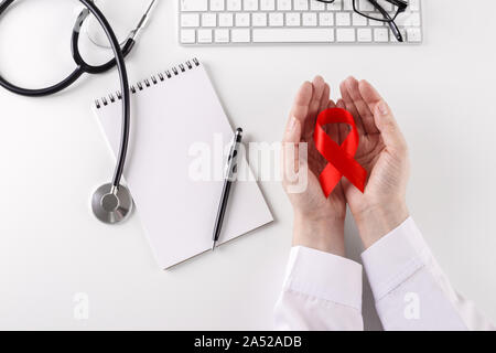 Doctor holding ruban rouge dans les mains la journée mondiale contre le cancer concept ,coin au bureau avec clavier lunettes stethoscope Banque D'Images