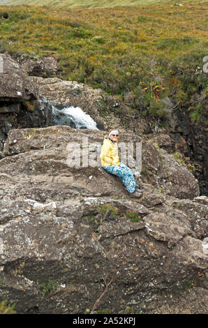 Un touriste assis sur un gros rocher par une petite chute d'eau à la célèbre conte de piscines, par Glen cassante, île de Skye, Écosse, Royaume-Uni, Europe. Banque D'Images