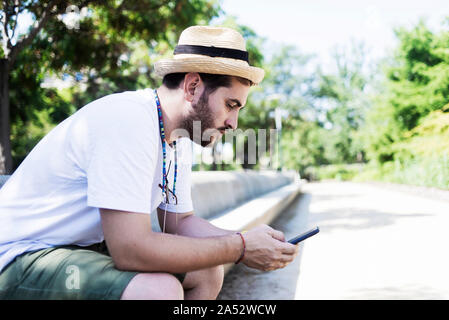 Jeune homme barbu assis sur un banc à l'aide d'un smartphone Banque D'Images