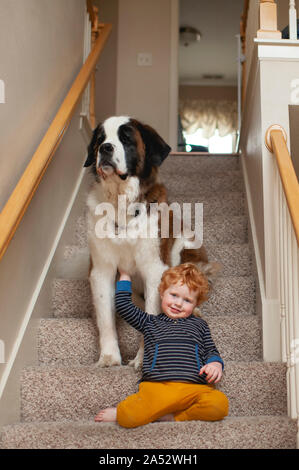 Bébé garçon souriant et s'appuyant sur grand chien à la maison sur l'escalier Banque D'Images