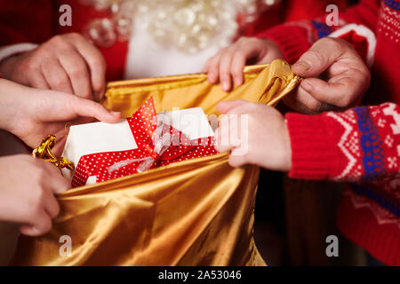 Le Père Noël ouvre un sac et donne des cadeaux aux enfants, assis près de l'arbre de Noël décoré avec des lumières - Joyeux Noël et bonnes fêtes ! Banque D'Images