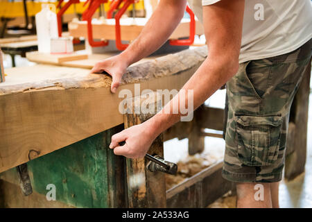 Carpenter serrant une planche de bois dans un étau ou vice sur un établi dans un atelier de menuiserie dans un gros plan sur ses mains Banque D'Images