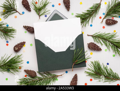 Joyeux Noël et Bonne Année carte dans l'enveloppe. Note blanche feuille de papier. Décor de branches de pins, de cônes et de confettis de fête Banque D'Images
