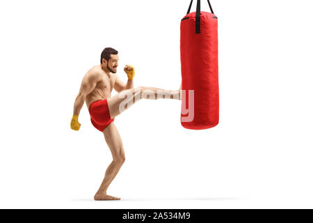 Profil de pleine longueur de balle un jeune homme musclé l'exercice de kickboxing et sac de frappe un coup avec sa jambe isolé sur fond blanc Banque D'Images