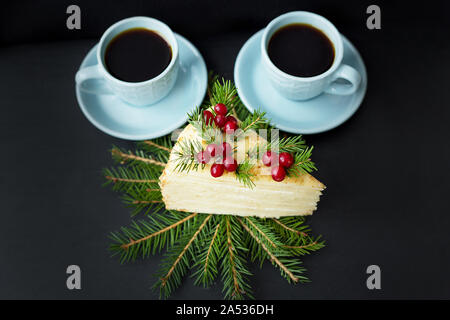 Morceau de gâteau décoré arbre et fruits rouges sur un fond noir avec deux tasses de café. Banque D'Images