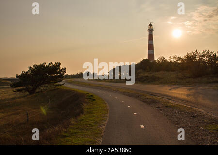 Lever du soleil derrière les genets, le phare d'Ameland, avec rue menant vers l'édifice Banque D'Images