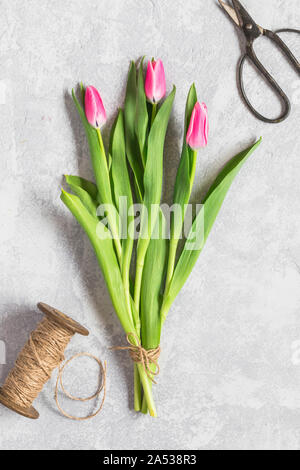 Un simple bouquet de tulipes sur fond gris, vu de dessus.Les trois tulipes sont roses et sont attachés ensemble par une corde de jute. Il y a un tiroir et un p Banque D'Images