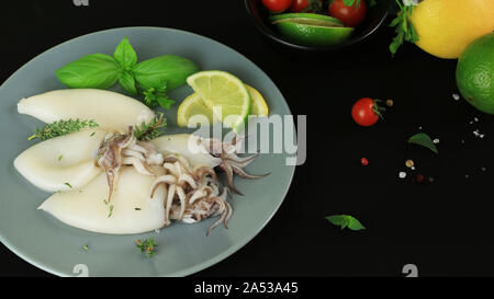 La plaque avec le calmar frais avec du citron et des herbes sur fond sombre Banque D'Images