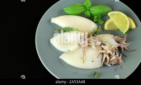 La plaque avec le calmar frais avec du citron et des herbes sur fond sombre Banque D'Images