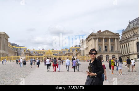 Versailles, Ile de France / France - 21 juin 2016 : Chinese female tourist ressemble à l'appareil photo, des foules de touristes mill à propos du Palais de Versailles Banque D'Images