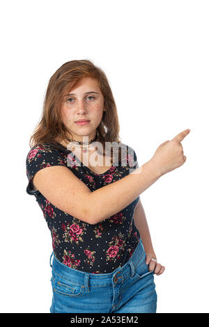 Studio shot verticale d'une re-teen girl with freckles dirigée vers la droite avec sa main droite. L'expression grave. Fond blanc avec copie espace Banque D'Images