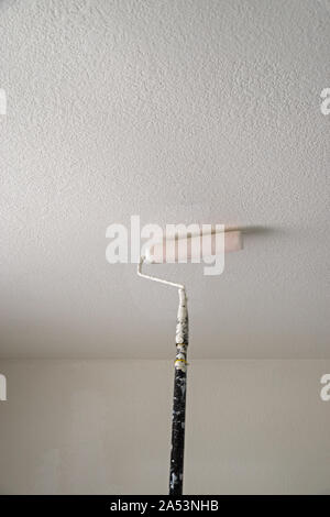 Peinture d'un plafond texturé blanc avec un rouleau à peindre sur un poteau avec un effet de flou Banque D'Images