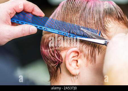 Gros plan du salon de coiffure coupe de cheveux rose humide du client dans le salon. Hairstylist coupe woman's hair. Vue latérale des mains sont la coupe de cheveux avec des ciseaux. Banque D'Images