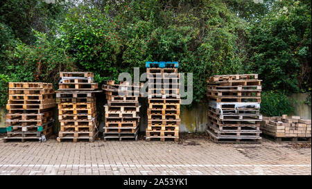 Des piles de palettes en bois dans une cour pavée block builders entouré de verdure des arbres sur l'image Banque D'Images