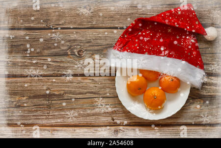 Arrière-plan en bois avec mandarines sur l'assiette à l'intérieur du chapeau de Noël sur la table. Cadre vacances d'hiver. Vue de dessus de la couche à plat. Espace de copie Banque D'Images