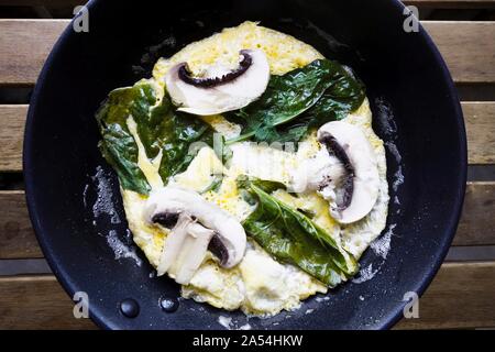 Omelette aux épinards et champignons dans une casserole sur la table. Banque D'Images