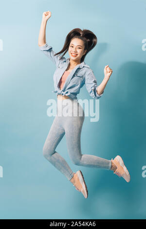 Portrait de jeune fille fou ludique sautant en l'air à la caméra à profiter de week-end avoir parfaite humeur sur fond bleu clair Banque D'Images