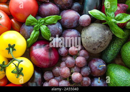 Différents types de fruits et légumes, vue d'en haut. Violet lumineux les raisins, les pruneaux, coloré en vert à l'avocat et les feuilles de basilic. Tomates jaunes. Banque D'Images