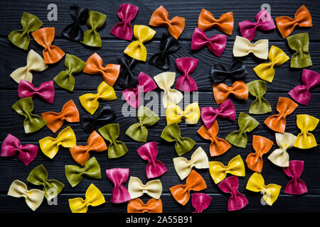 Assortiment de farfalle ou farfalline rustique en bois sur fond noir. La cuisine italienne. Rose, vert, rouge, violet, jaune et orange. Banque D'Images