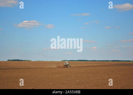 Tracteur semer le grain dans le domaine de terre noire, sunny blue sky, Ukraine Banque D'Images
