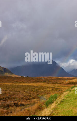 Un arc-en-ciel entre le soleil, la lande de Rannoch Moor et les montagnes couvertes de nuages sombres des Trois Soeurs, ou Bidean nam Bian à Glencoe. Banque D'Images