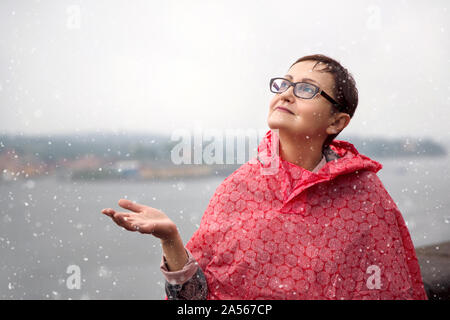 Femme d'âge moyen de regarder le ciel sur une journée d'hiver enneigée et dans l'espoir d'un Noël blanc. Une scène d'hiver. Tempête de neige météo Banque D'Images