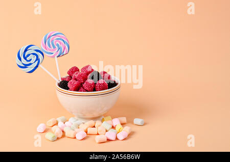 Sweet gummy dans la cuvette et de la guimauve sur fond orange pastel. Banque D'Images