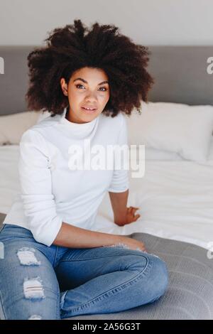 Jeune femme avec coiffure afro sitting on bed, portrait Banque D'Images