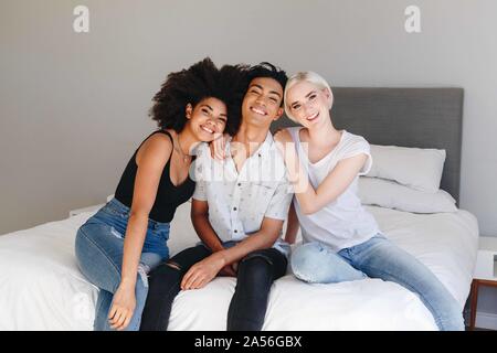 Heureux jeune homme et deux femmes friends sitting on bed, portrait Banque D'Images