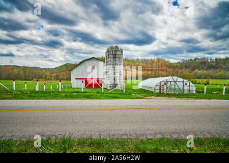 Red Roof barn et silo le long d'une route de campagne. Banque D'Images