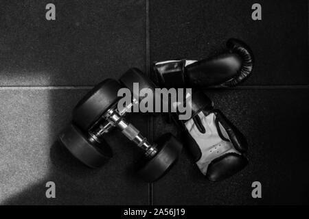 Deux haltères pour la remise en forme et le noir et blanc des gants de boxe sur le sol en caoutchouc. Banque D'Images