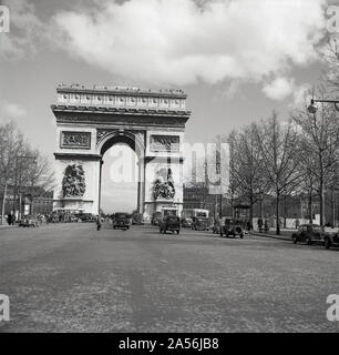 Années 1950, historique, voitures de l'époque sur une rue pavée menant à l'Arc de Triomphe, situé sur la place de Charles de Gaulle, Paris, France. Ouvert en 1836, le célèbre monument a été construit pour honorer ceux qui ont combattu et sont morts pour la France pendant la Révolution française et les guerres napoléoniennes. Banque D'Images