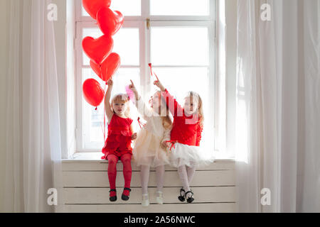 Trois petites filles s'assoient près de la fenêtre avec des ballons Banque D'Images