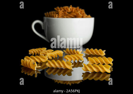 Beaucoup d'ensemble complet de fusilli secs brown tasse en céramique blanc isolé sur verre noir Banque D'Images